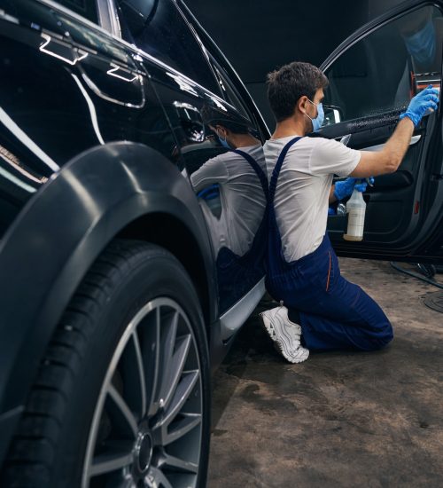 Man in repair workshop washing car window during car valeting