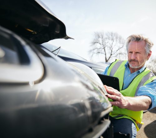 Mature Male Loss Adjuster With Digital Tablet Assessing Insurance Claim In Car Pound